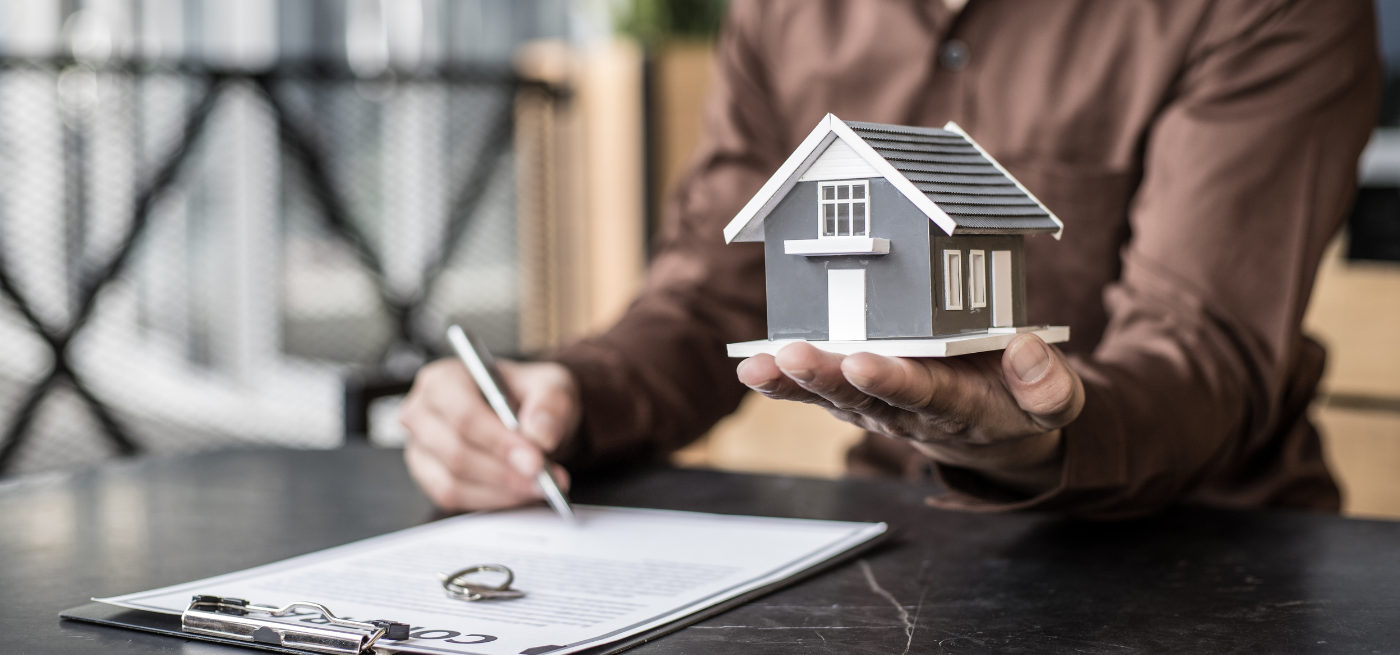 Pessoa a assinar um contrato enquanto segura uma casa em miniatura